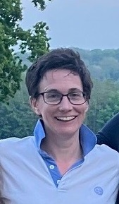 A woman with short brown hair and glasses looks out at the camera smiling. She has a Girlguiding shirt on