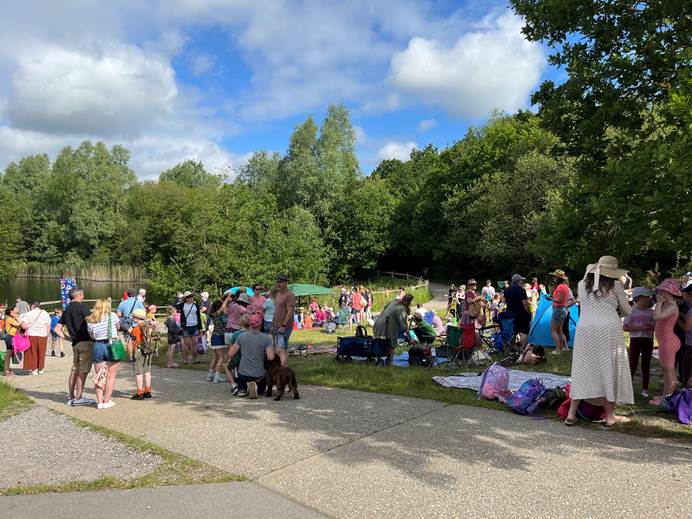 Brownies and their parents and leaders standing together in a park on the edge of water, waiting for the Regatta to start.