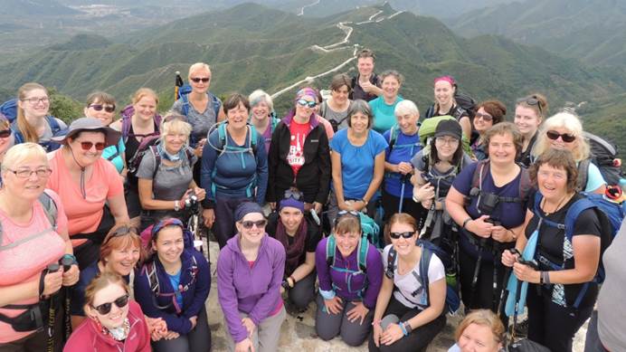 Group of Great Wall of China trekkers standing on top of a hill with the Wall in valley behind them