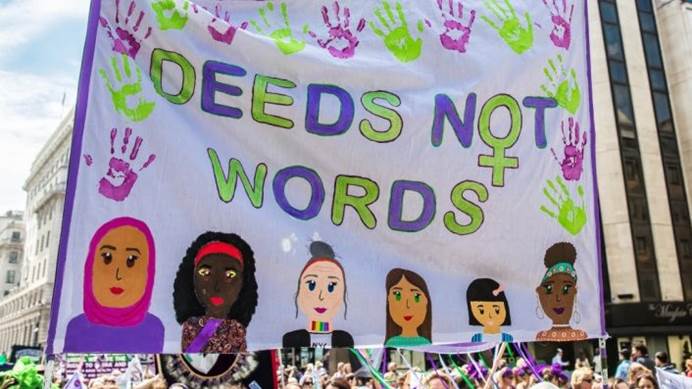 The Guides' banner at the Processions march held above the crowd, featuring the slogan "Deeds not words"