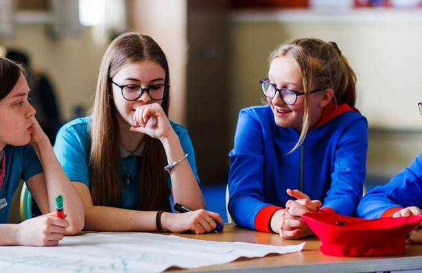 4 young leaders are sat aorund a table with a map in front of them, laughing and having a conversations.