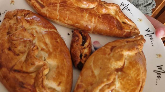 A young girl holding a plate with 3 homemade pasties on. 