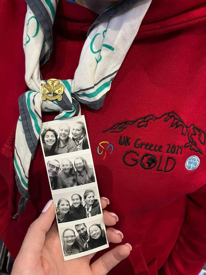 Holding up a string of photo booth images of members of the two teams smiling in front of a UK Greece 2024 Gold top and necker