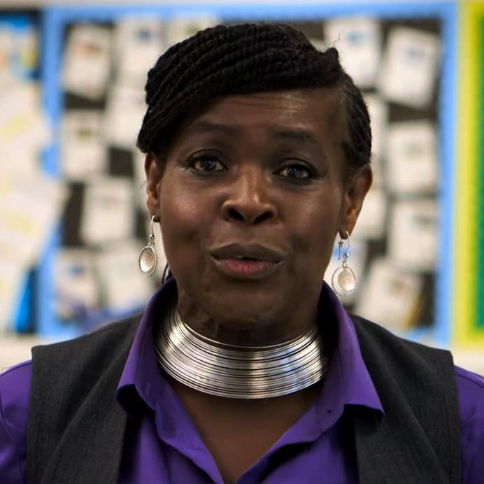 A photograph of Dame Margaret Aderin-Pocock with colourful display boards in the background.
