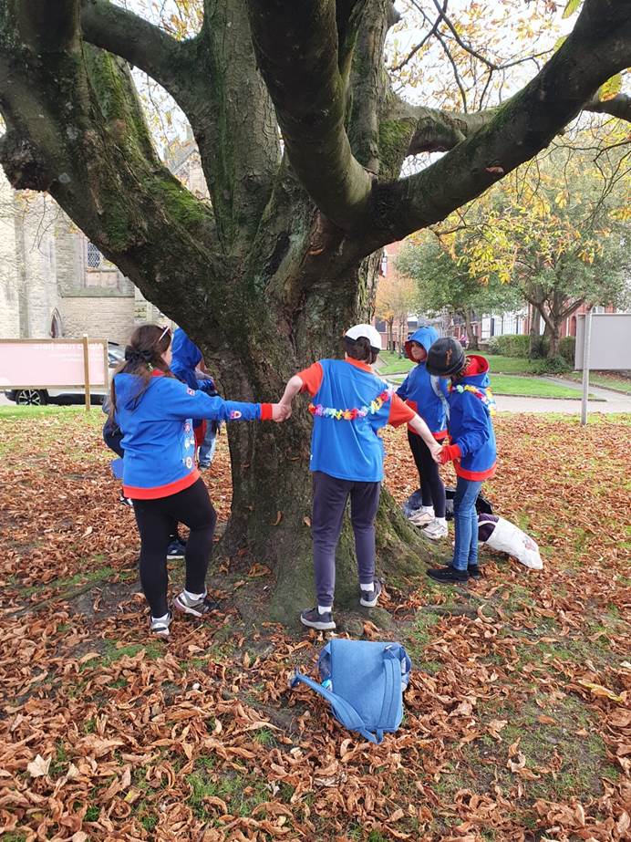 Guides hold hands around a tree trunk in a park forming a circle around it.