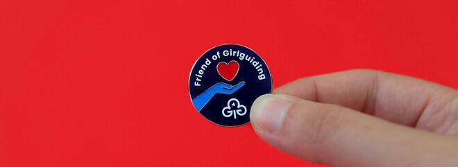A round badge with a hand holding a heart, with the Girlguiding logo below and the words 'Friend of Girlguiding' above.
