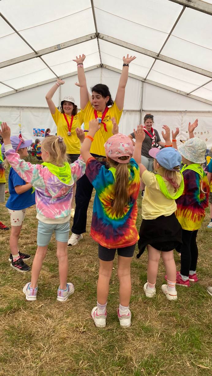Two team members lead a workshop with young girls wearing tie dye t-shirts in a tent