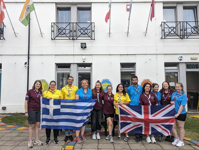 The Greece and UK project teams holding their national flags and standing in front of Pax lodge