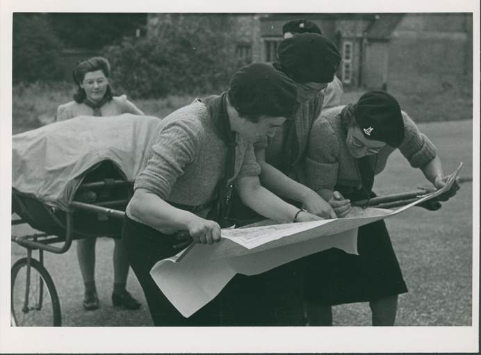 Guides in GIS training in 1943. They are standing next to a trek cart, reading a map.