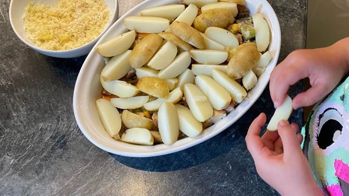 A large dish of uncooked potato wedges and a bowl of grated cheese