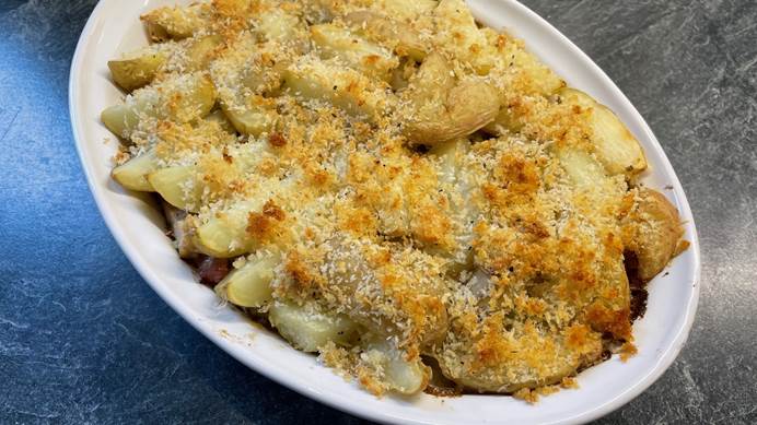 A large white dish containing potatoes with a crispy cheesy topping