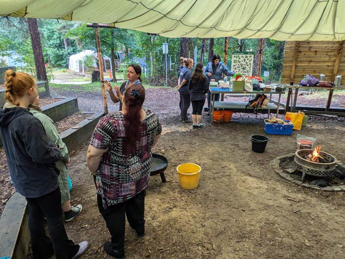Girlguiding leaders stand under a tarpaulin in the forest with a bushfire going ready to learn how to create a bushfire