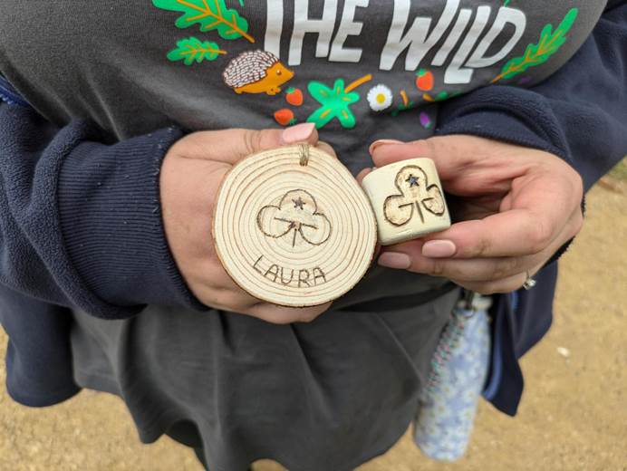 A leader holds two circular wooden decorations have a Trefoil engraved on them using Pyrography. One of them also says Laura underneath.