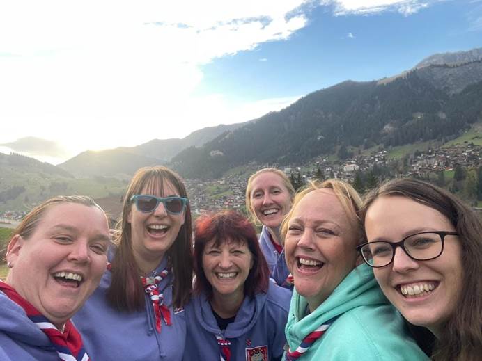 6 women smile at the camera. The photo is a selfie. Behind them is the village of Adelboden and hills