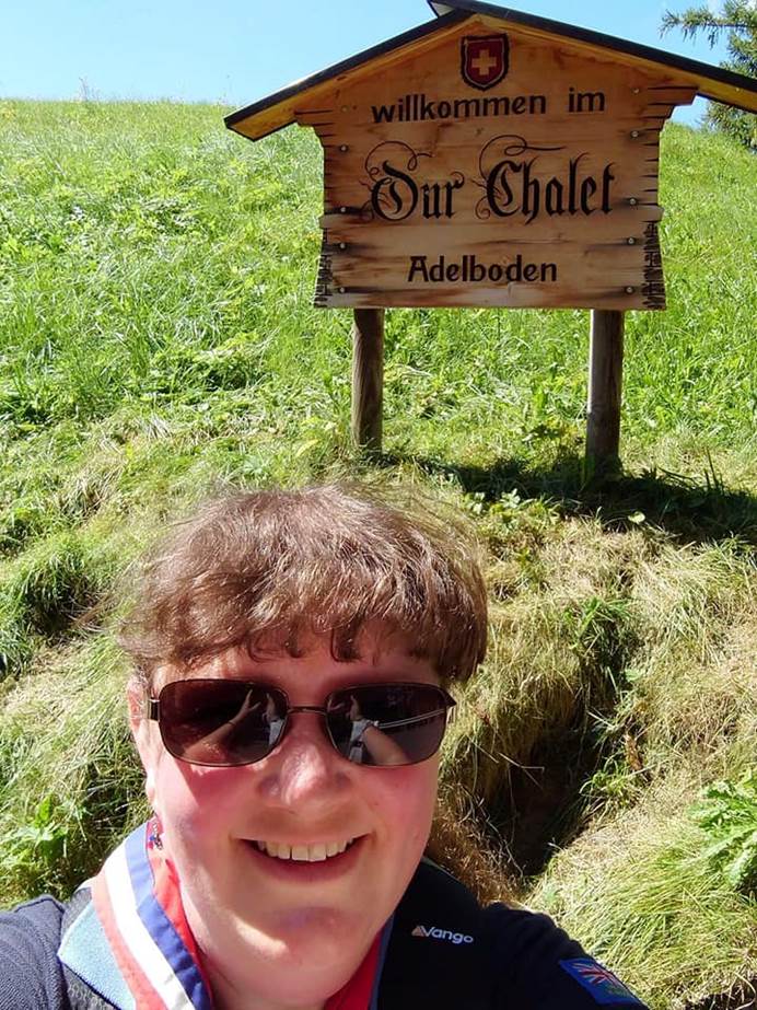Sharon takes a selfie, smiling at the camera while wearing sunglasses. Behind them is the Our Chalet sign, which willkommen, welcome in German