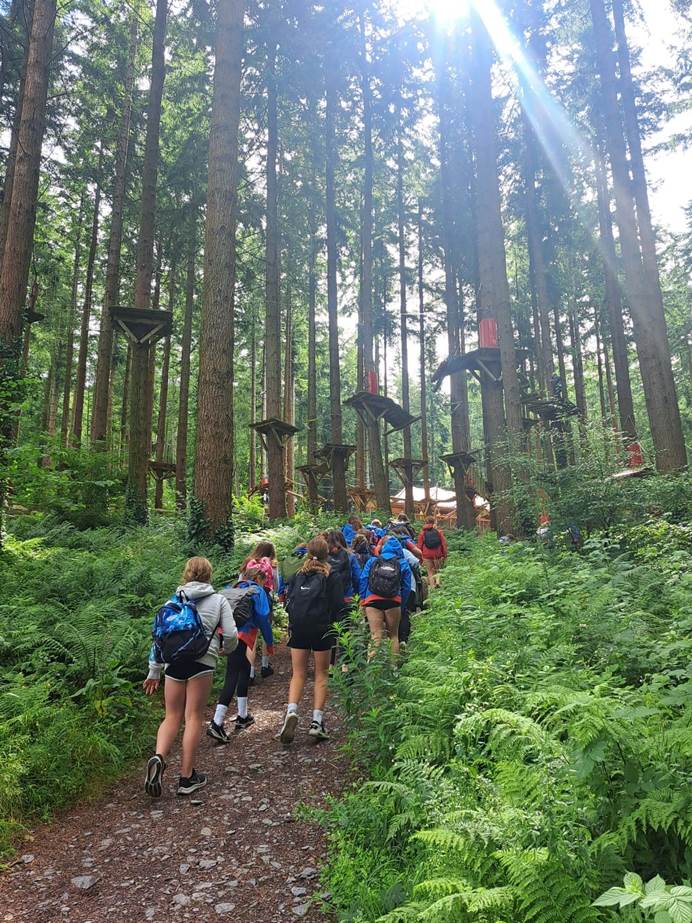 A group of in Guides in uniform walking up into the forest towards Zip World