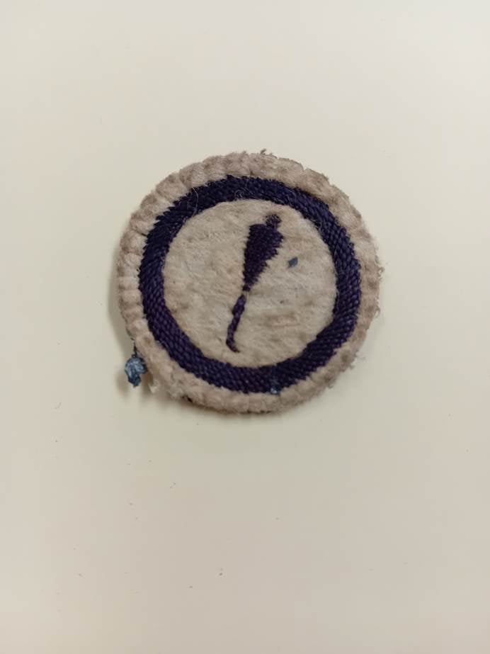 Round white felt badge with embroided cobbler's tool on the front.