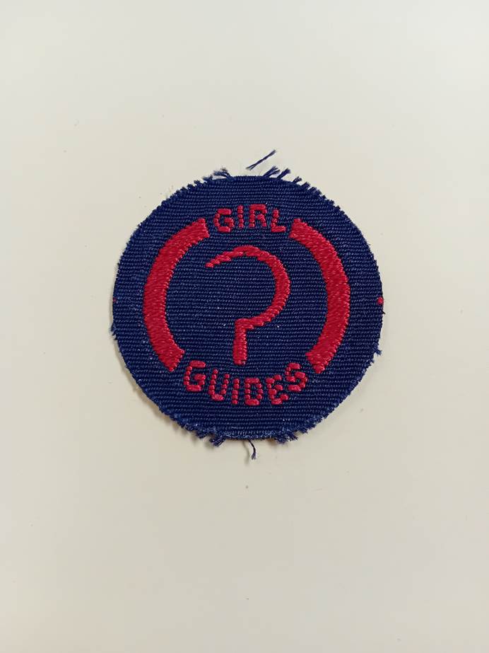 Round navy woven badge with a red embroided farmer's tool on the front.