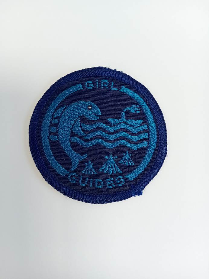 Circular, dark blue badge with embroided sea, boat, fish and tepees