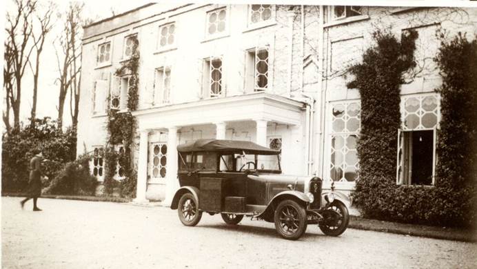 Black and white photo of manor house with classic car parked in front