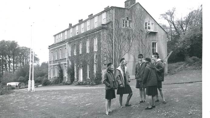 Black and white image of girl guides standing in front of Waddow Hall chatting to each other