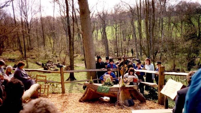 Group of girls and volunteers in guiding uniform playing musical instruments outdoors and holding songsheets. Backdrop is of a wooded farm