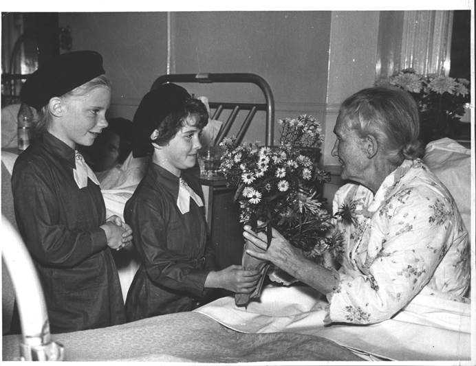 Black and white image of Brownies giving a patient flowers on a hospital visit, 1967