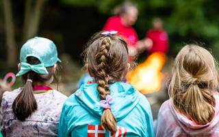 Three girls with their backs to the camera are facing towards a campfire