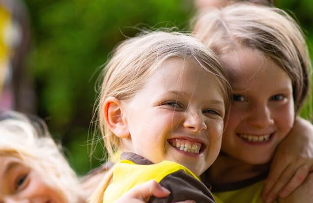 Two Brownies, wearing uniform, hug and smile at the camera. They're white, have blonde hair and are wearing uniform