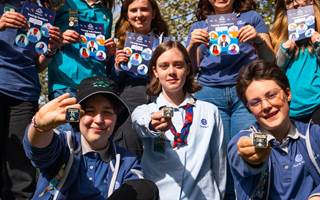 The young leader working group, a group of young people aged between 14-18, are standing outdoors in a green area and smiling at the camera. They're all wearing the mid blue young leader uniform and some of them are holding badges.