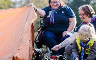 Two volunteers and one girl in Brownie uniform are assembling a tent outdoors