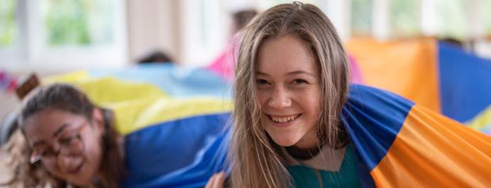 Two Rangers are smiling at the camera from underneath a colourful indoor parachute. 