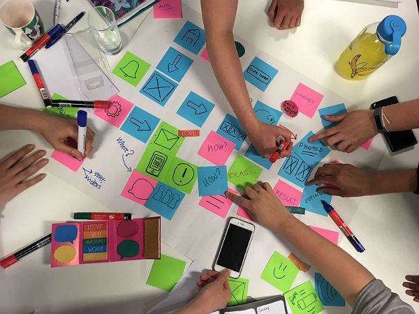 Birds eye view of people writing on colourful sticky notes laid out on a table