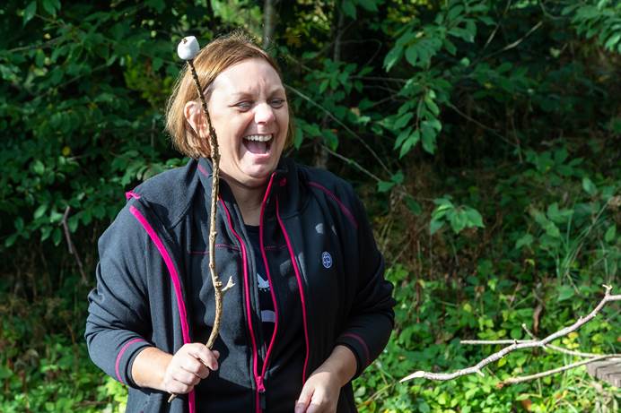 A Girlguiding leader laughs while holding up a toasted marshmallow on a stick