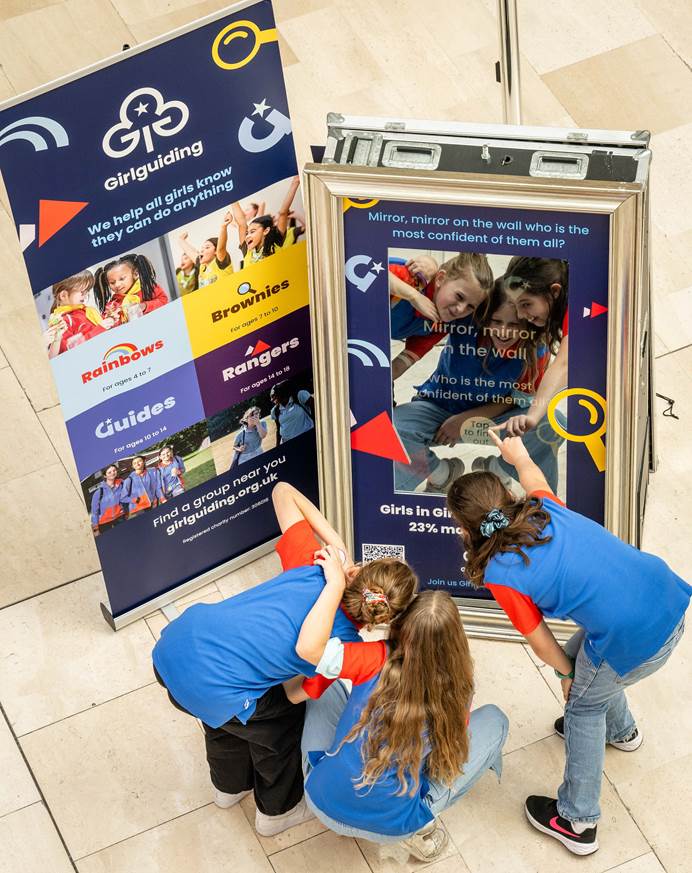 3 guides in uniform look into a mirror which reads "mirror mirror on the wall, who is the most confident of all? Girls in Girlguiding are up to 23% more confident"